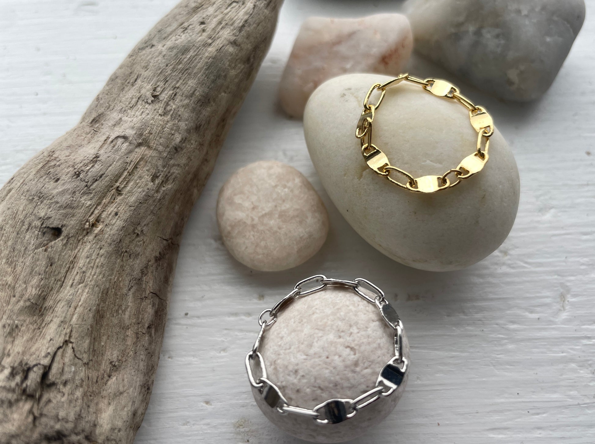 Photo of chain ring stack featuring both silver and gold variants, set against a background reminiscent of Costa del Sol. The rings display intricate chain designs, gleaming with elegance and sophistication.